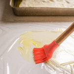 Greasing a piece of plastic wrap with olive oil to put on top of the focaccia dough.