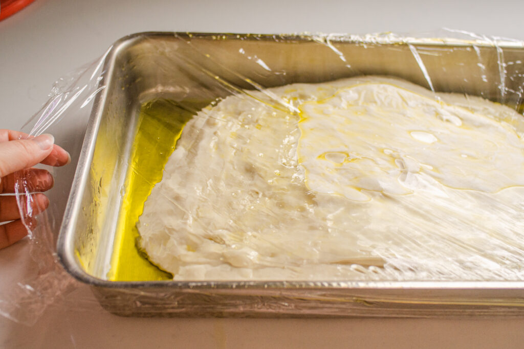 The sourdough focaccia rising in the pan with plastic wrap on top.