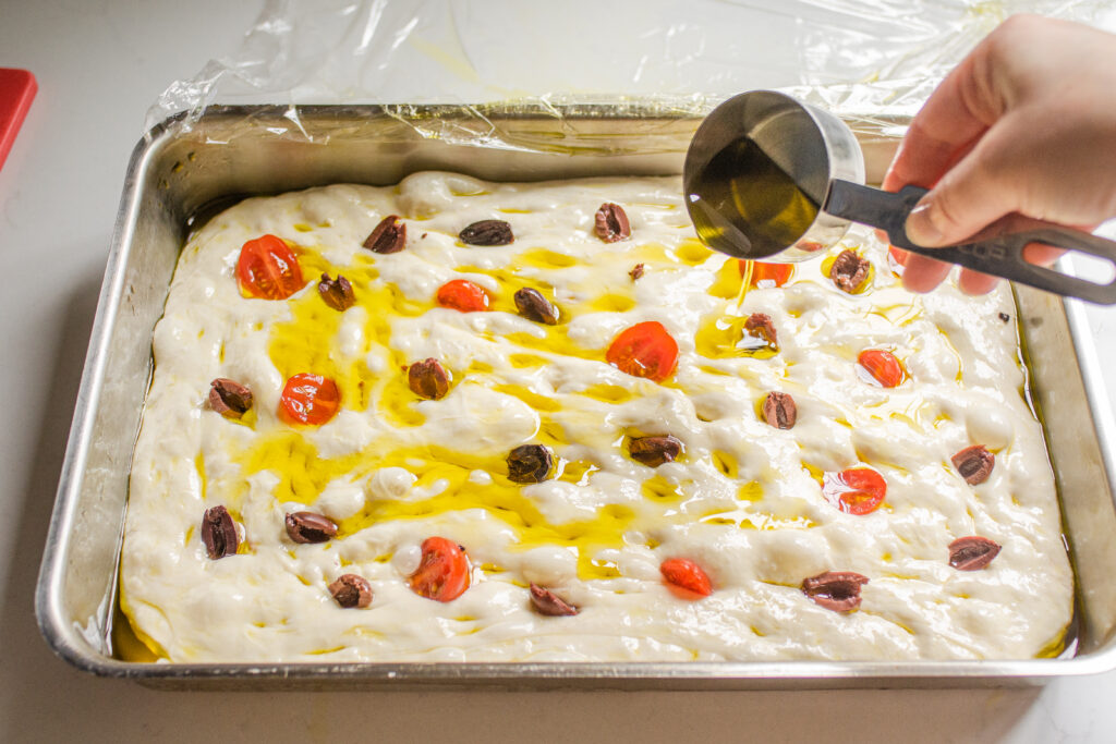 Pouring extra virgin olive oil over the toppings on the focaccia dough.