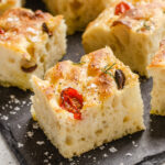 Pieces of sourdough focaccia on a slate board with flaky sea salt and freshly ground pepper.