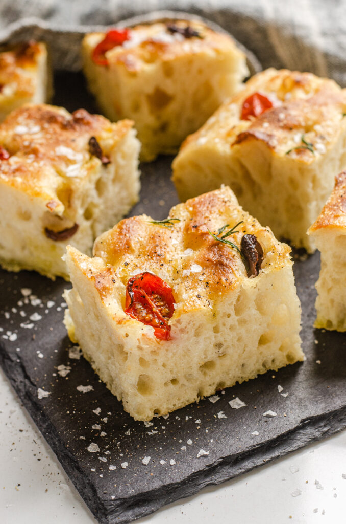 Pieces of sourdough focaccia on a slate board with flaky sea salt and freshly ground pepper.