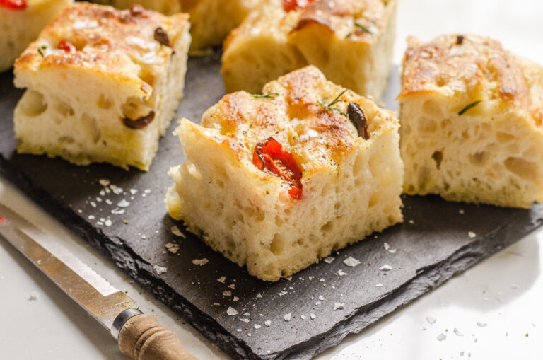 A side shot of a sliced piece of sourdough focaccia o a slate board so you can see the open crumb.