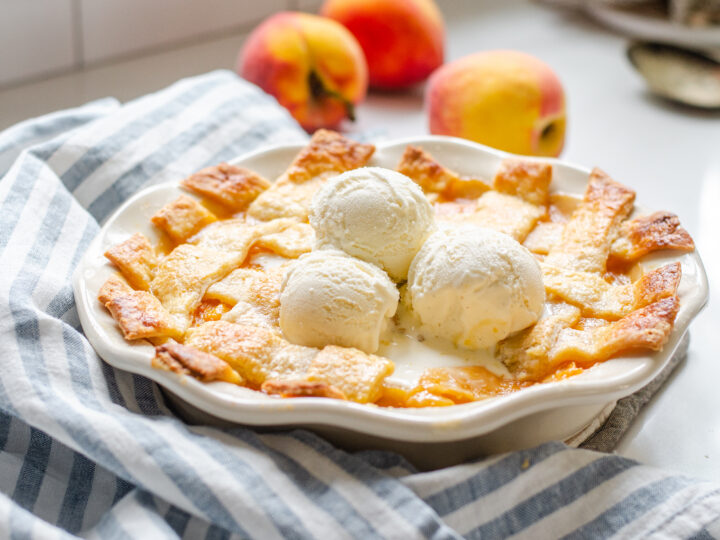 A southern peach cobbler baked in a pie dish with a lattice pie crust topping.