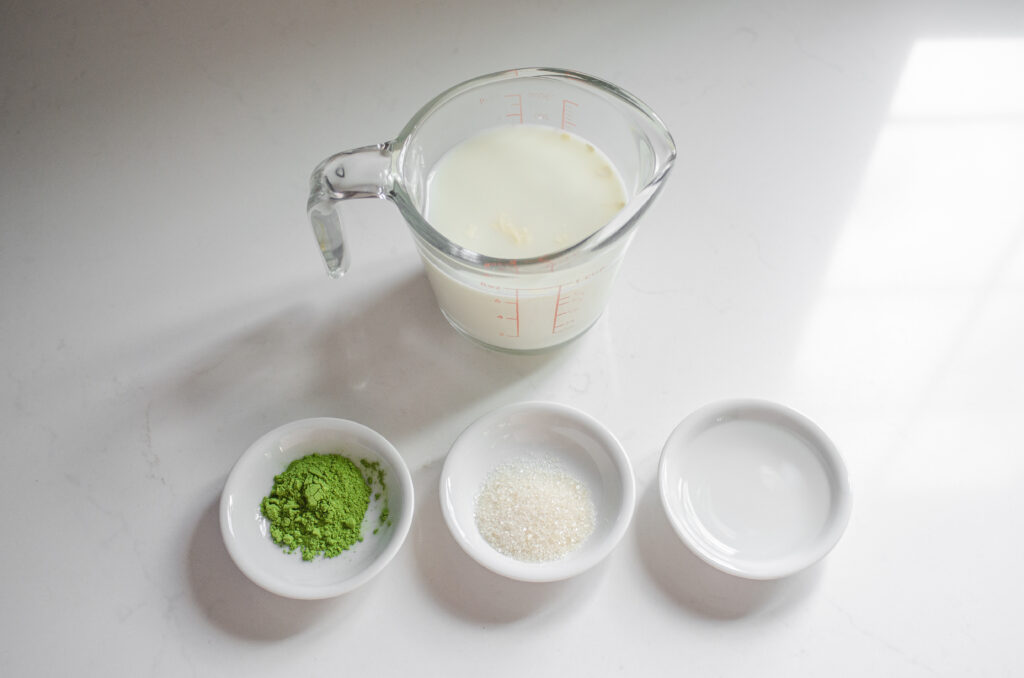 All of the ingredients needed to make a Starbucks hot matcha green tea latte laid out on a white countertop.