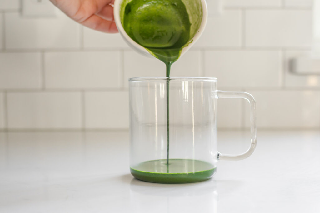 Pouring the whisked matcha and sugar mixture into a separate mug.