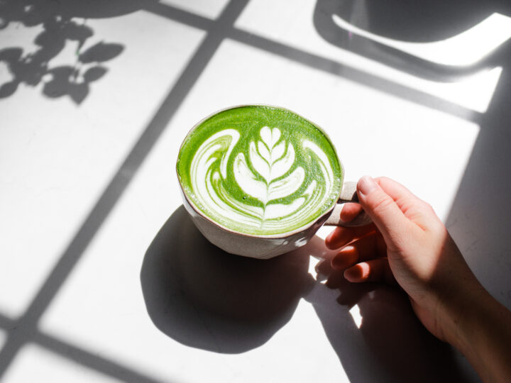 Holding a mug of homemade Starbucks hot matcha green tea latte on a sunny counter.