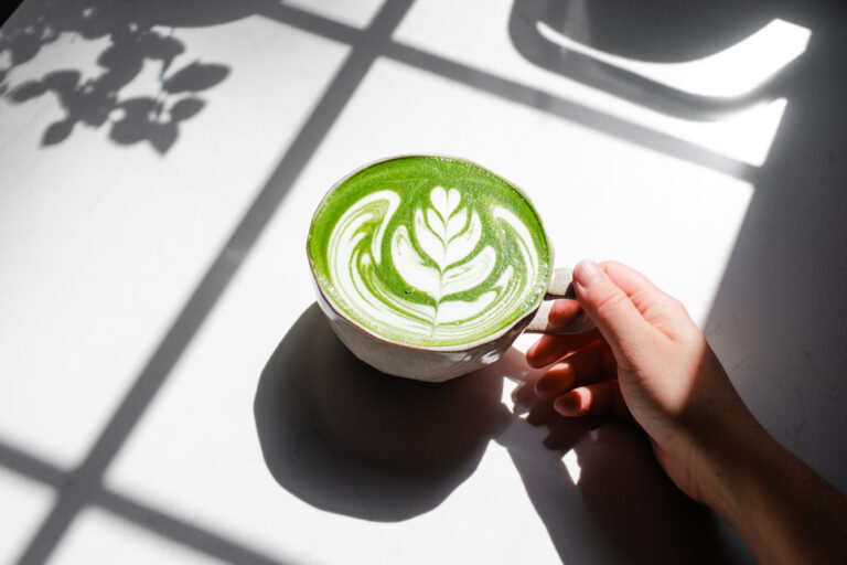 Holding a mug of homemade Starbucks hot matcha green tea latte on a sunny counter.