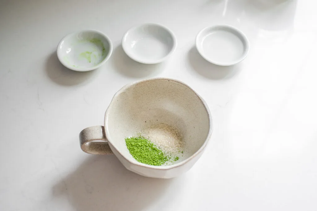 Matcha and sugar in a stoneware mug on a white countertop.