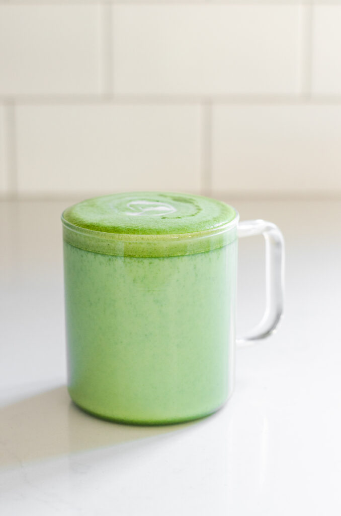 Starbucks copycat matcha green tea latte in a clear glass mug on a white countertop with subway tiles in the background.