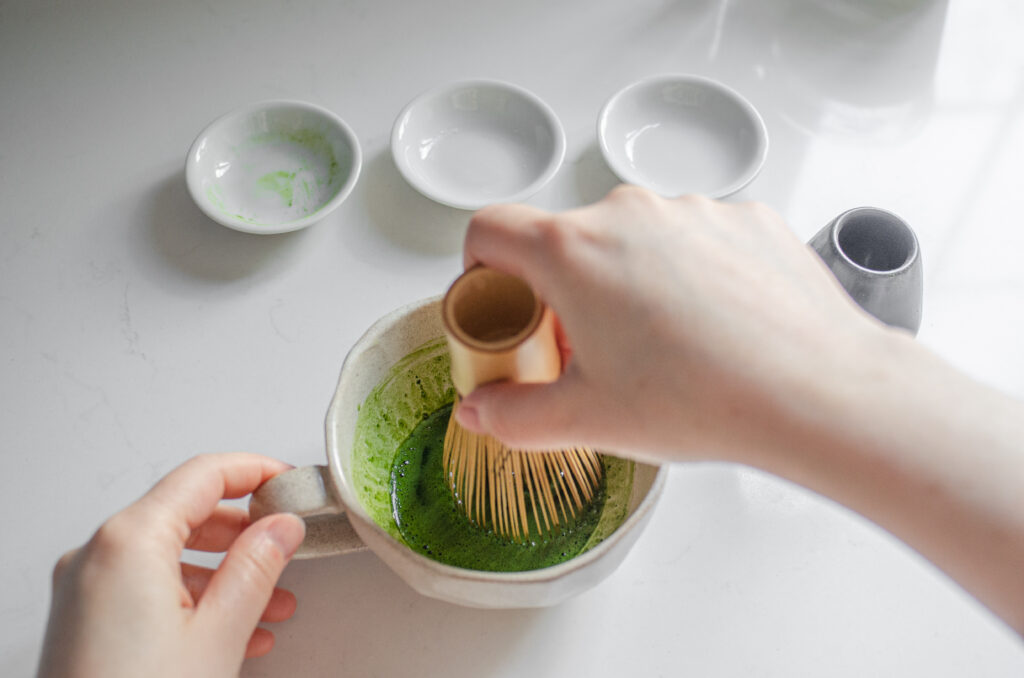 Whisking the matcha and sugar with hot water in a stoneware mug with a bamboo matcha whisk (chasen).