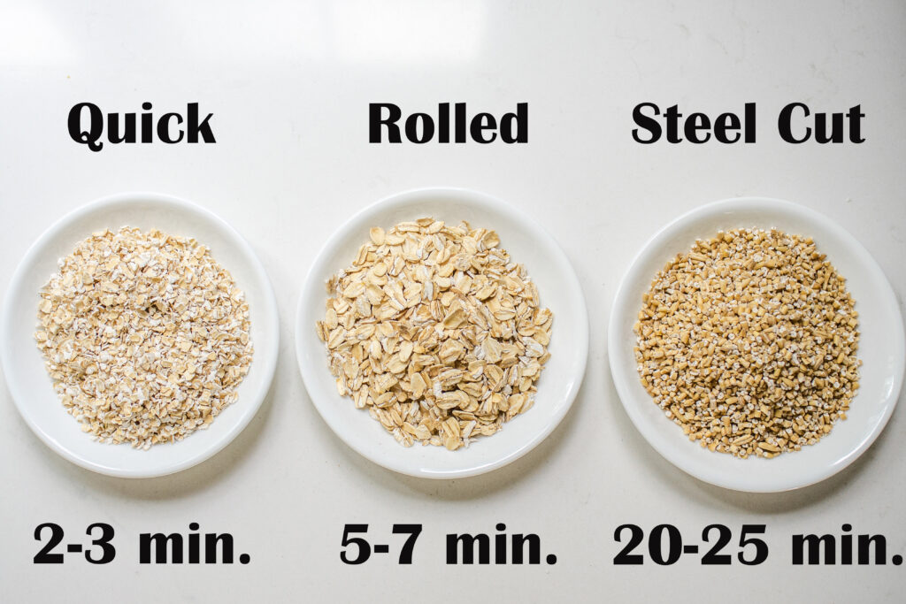 Quick cooking oats, rolled oats, and steel cut oats laid out in white bowls on a countertop.