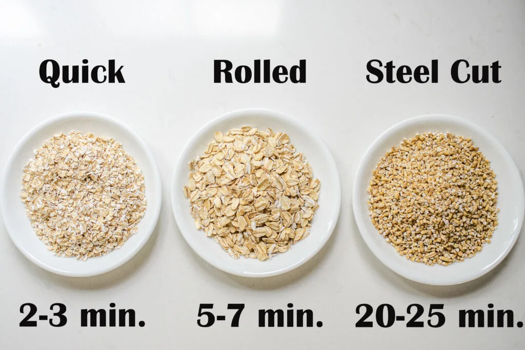 Quick cooking oats, rolled oats, and steel cut oats laid out in white bowls on a countertop.