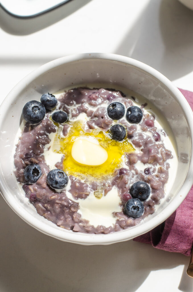 A bowl of blueberry oatmeal with cream, butter, and fresh blueberries on top.