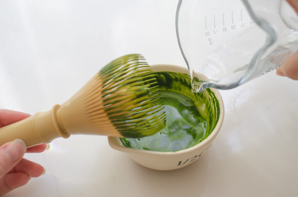 Whiskingg the matcha with hot water in a small spouted bowl to make matcha milk tea.