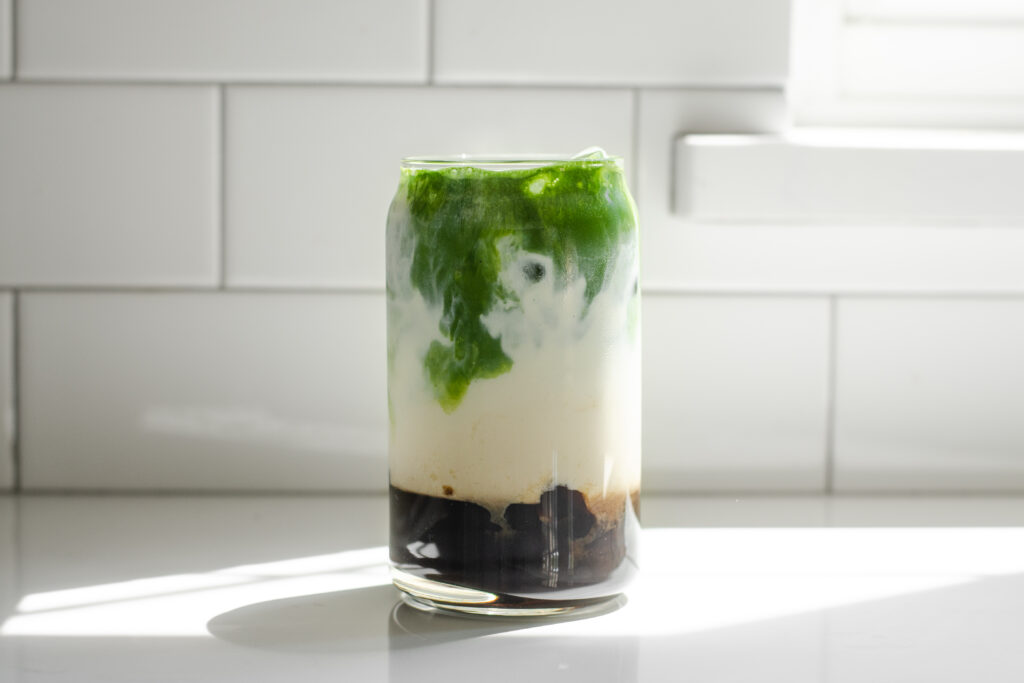 A glass of matcha milk tea on a white countertop in the sunlight.