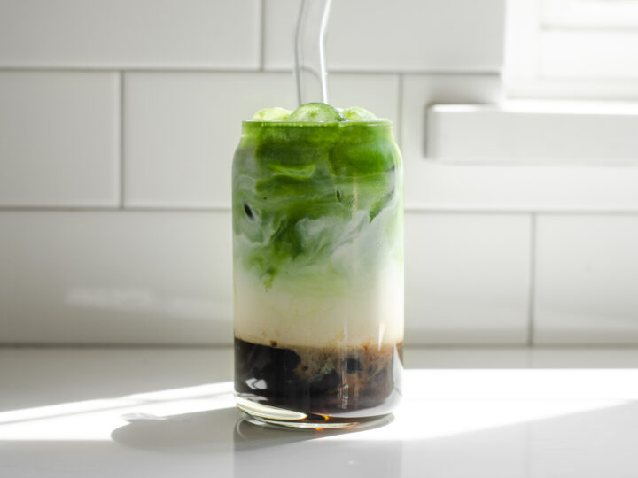 A glass of matcha milk tea on a white countertop in the sunlight.