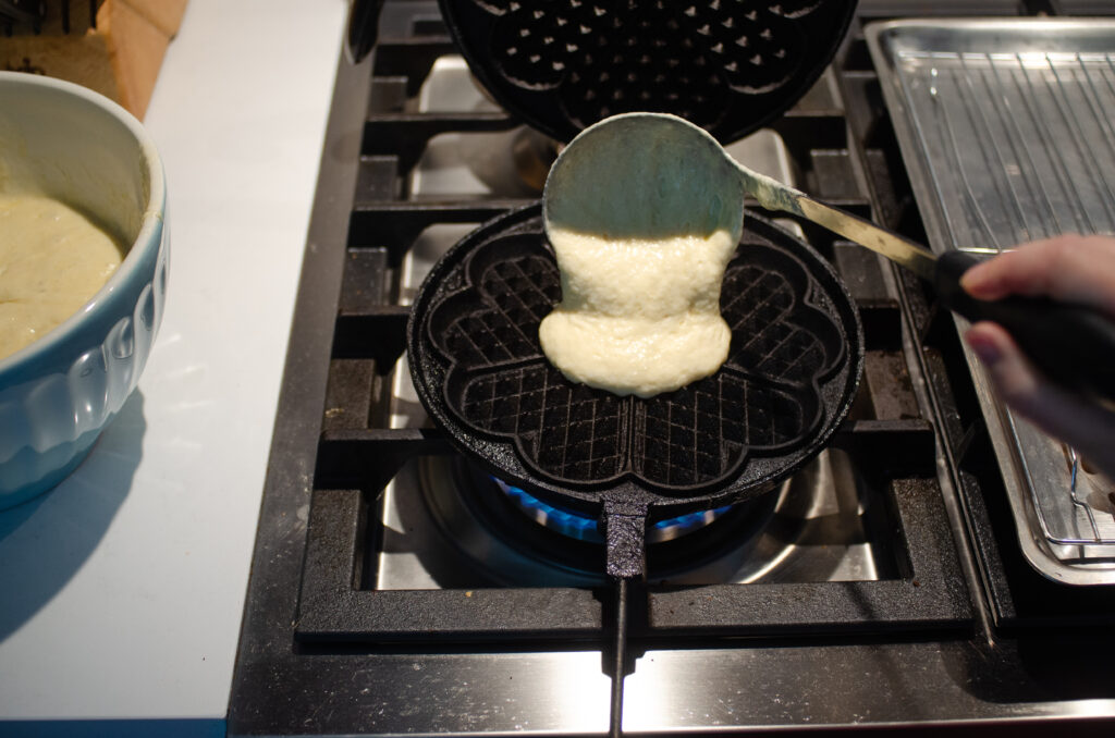 Using a ladle to transfer the waffle batter to the hot iron.