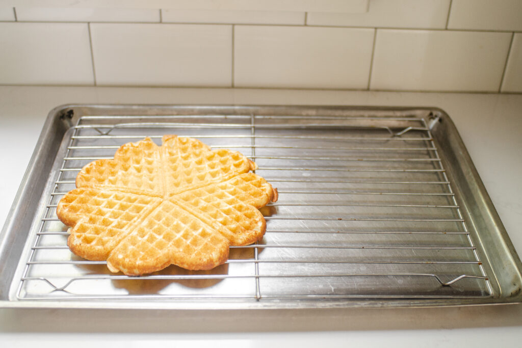 Placing a cooked sourdough discard waffle on a wire cooling rack on a baking tray. 