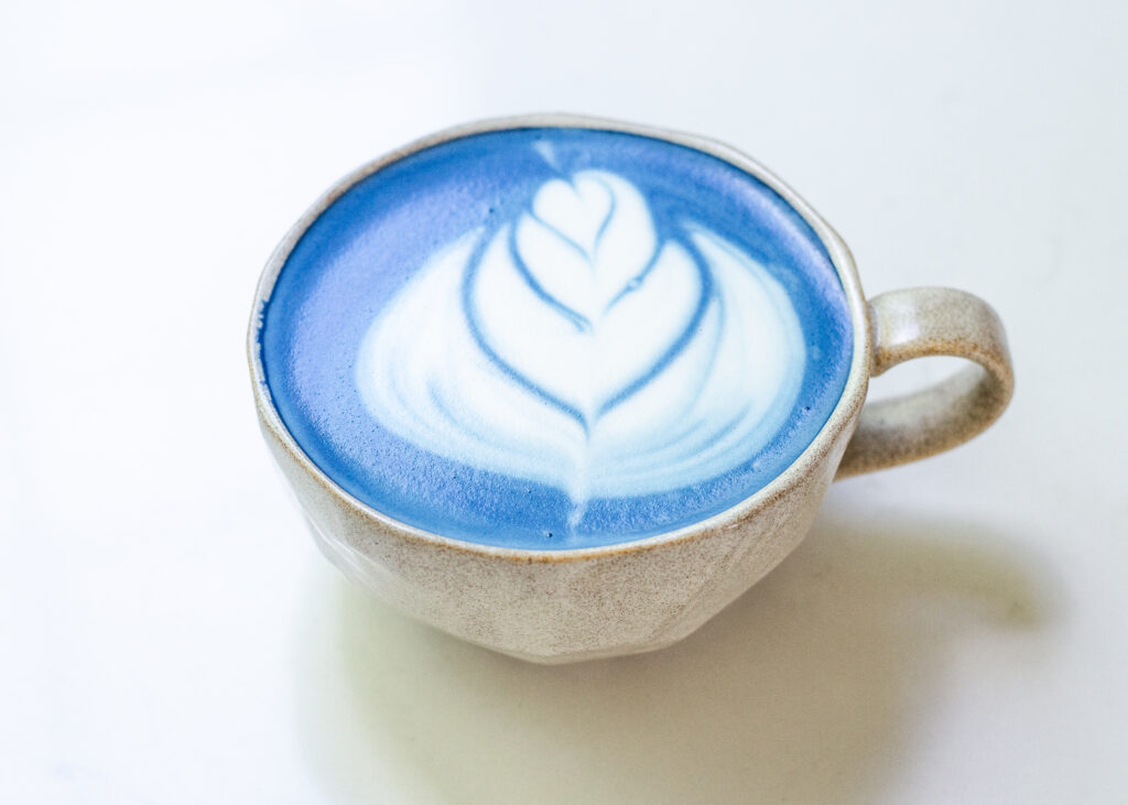 A mug of blue butterfly pea flower latte with latte art.