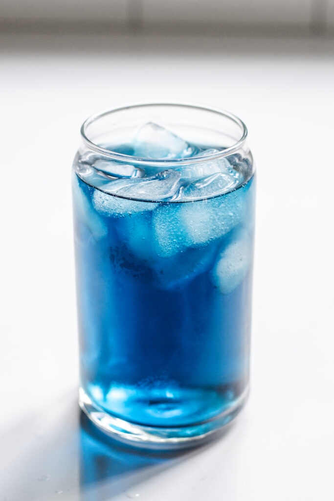 A 12 ounce glass of iced blue tea on a white countertop.