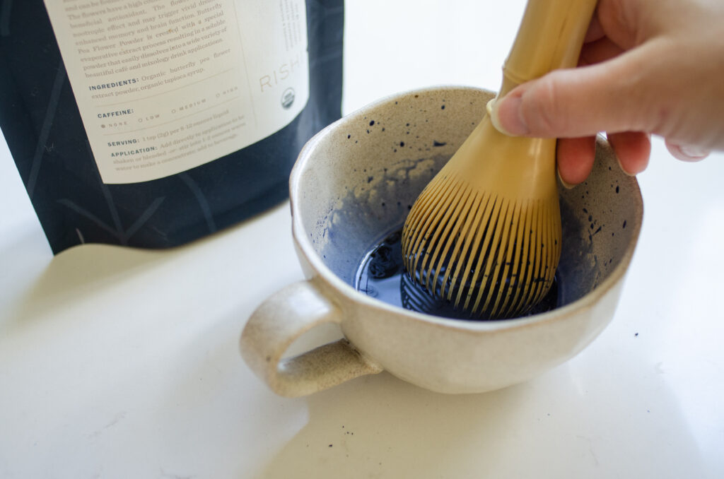 Whisking the blue butterfly pea flower powder with water in a mug to make a latte.