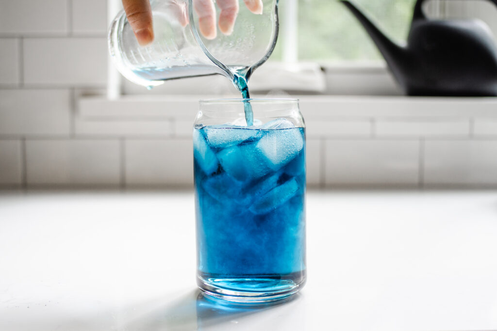 Pouring the brewed tea over the water and ice in the glass.