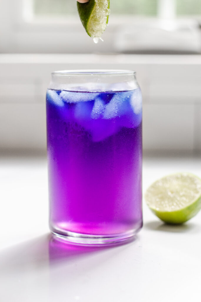 Adding lime juice to the iced butterfly pea flower tea.