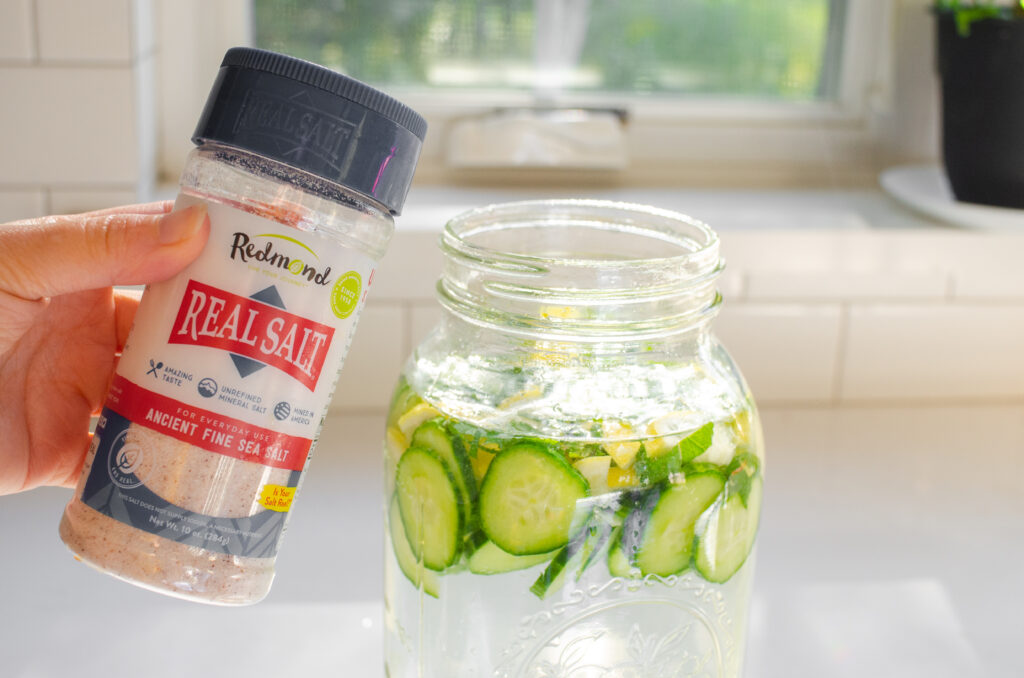 A shaker jar of Redmond real salt next to a jar of cucumber lemon mint water.