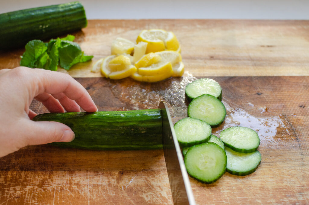 Slicing cucumbers, lemons, and mint on a wooden cutting board.