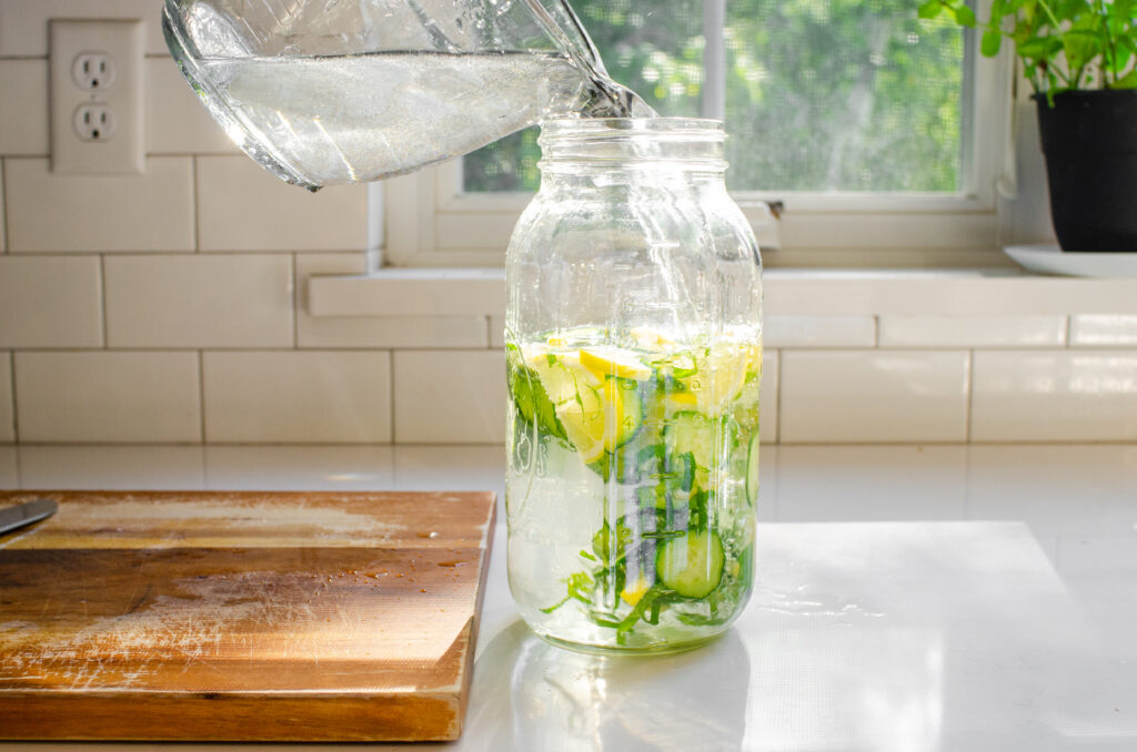 Pouring the water on top of the cucumber, lemon, and mint in the jar.