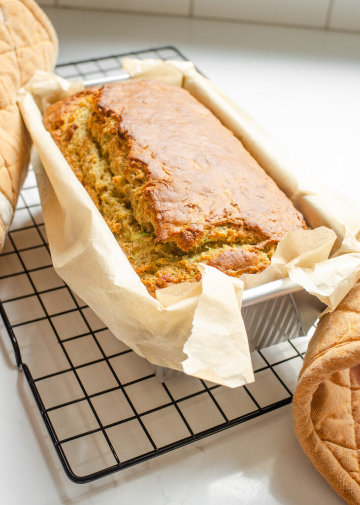 A baked loaf of banana zucchini bread on a cooling rack.