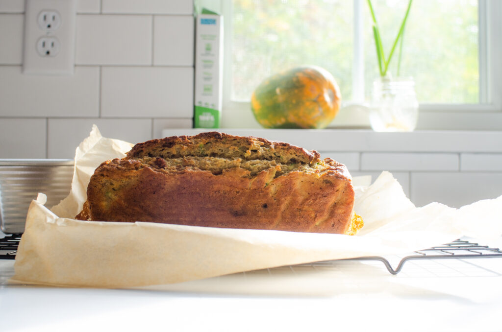 A loaf of banana zucchini bread cooling on a black wire cooling rack.