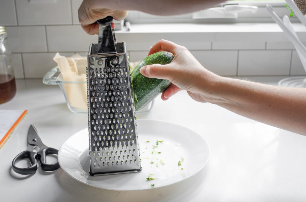 Grating zucchini using a box grater.