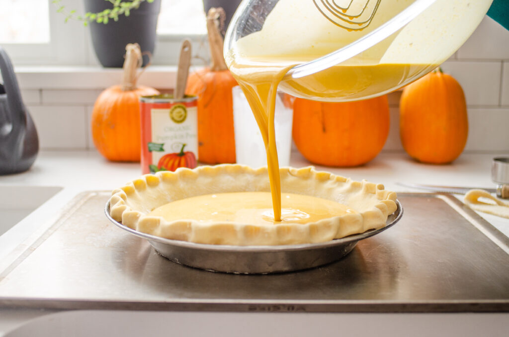 Pouring the pumpkin pie filling into the chilled pie crust.