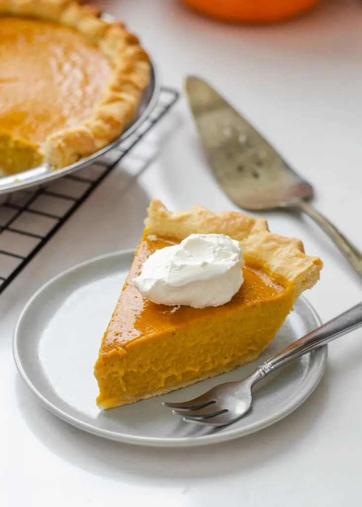 A piece of low sugar pumpkin pie on a plate with the rest of the pie in the background on a wire cooling rack.