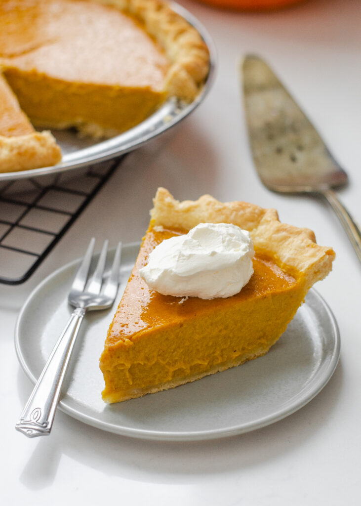 A piece of low sugar pumpkin pie on a plate with the rest of the pie in the background on a wire cooling rack.