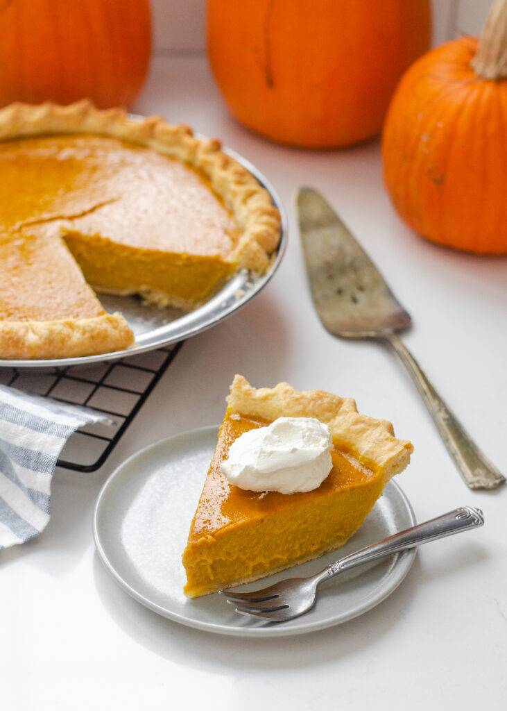 A piece of low sugar pumpkin pie on a plate with the rest of the pie in the background on a wire cooling rack.