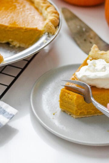 A piece of low sugar pumpkin pie on a plate with the rest of the pie in the background on a wire cooling rack.
