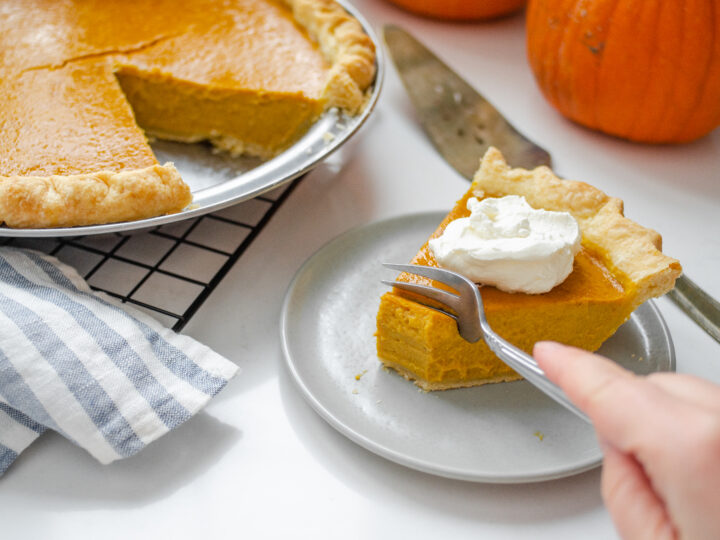 A piece of low sugar pumpkin pie on a plate with the rest of the pie in the background on a wire cooling rack.