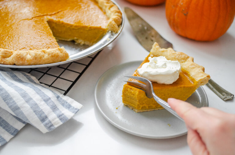 A piece of low sugar pumpkin pie on a plate with the rest of the pie in the background on a wire cooling rack.