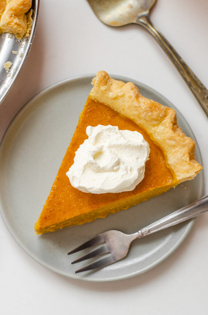 A piece of low sugar pumpkin pie on a plate with the rest of the pie in the background on a wire cooling rack.