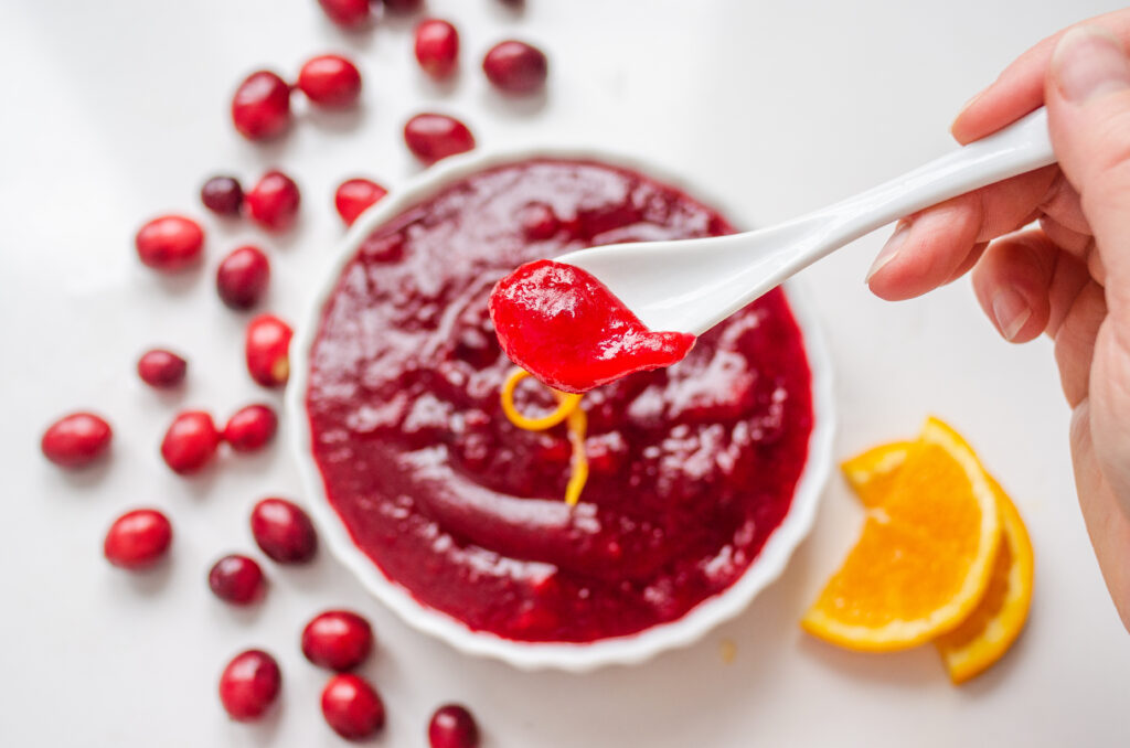 Holding a spoon of organic cranberry sauce with the dish of cranberry sauce blurry in the background.