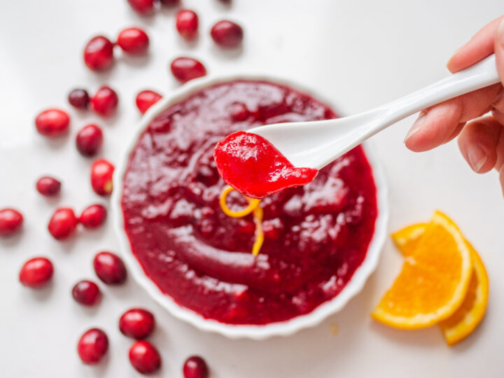 Holding a spoon of organic cranberry sauce with the dish of cranberry sauce blurry in the background.