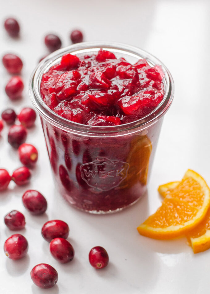 A jar of organic cranberry sauce with fresh cranberries and orange slices around it.