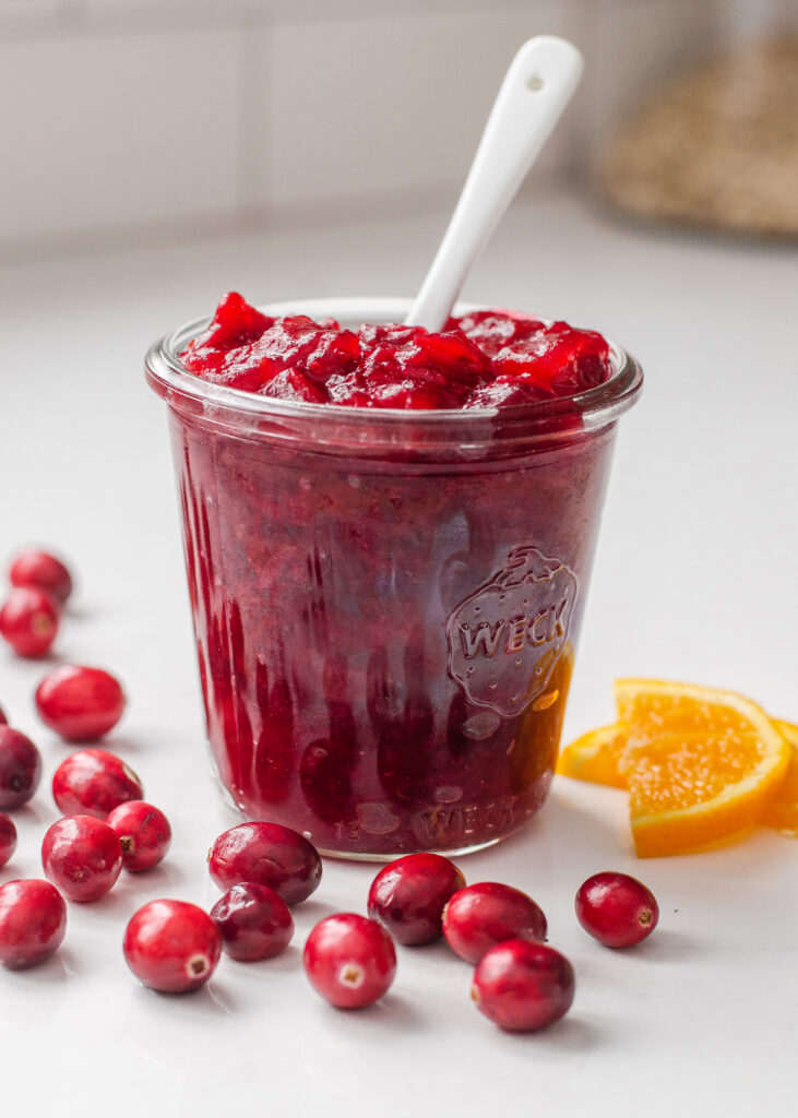 A jar of organic cranberry sauce with fresh cranberries and orange slices around it.