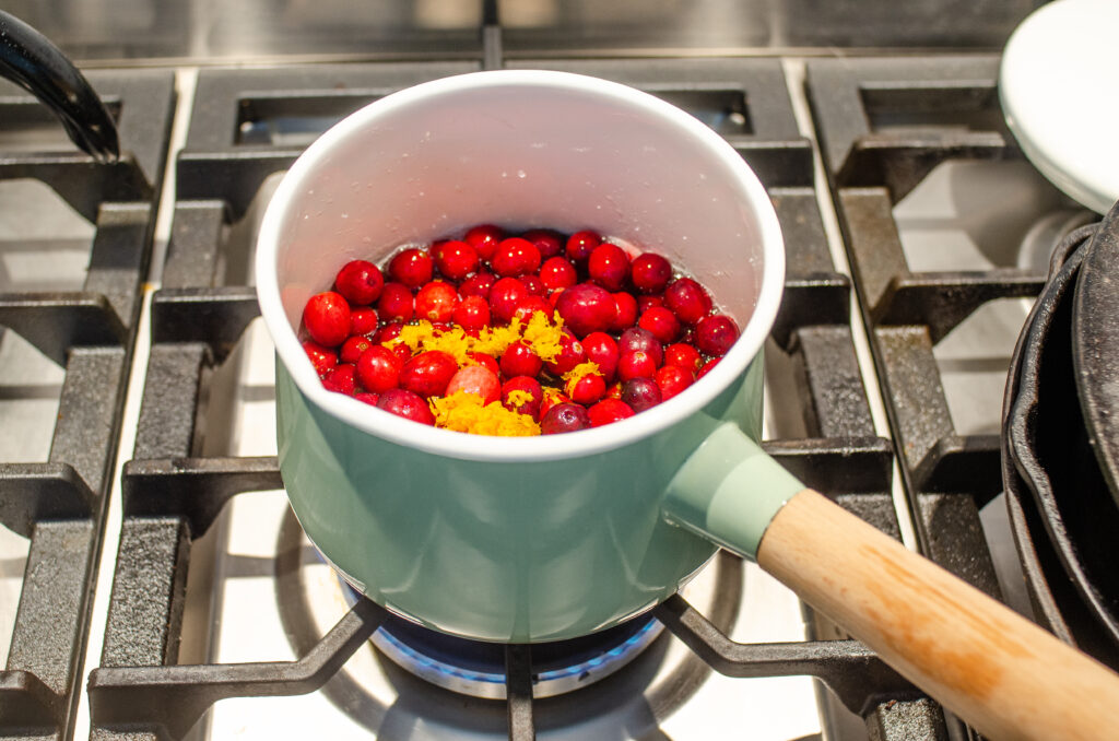 Adding the cranberries and orange zest to the saucepan.