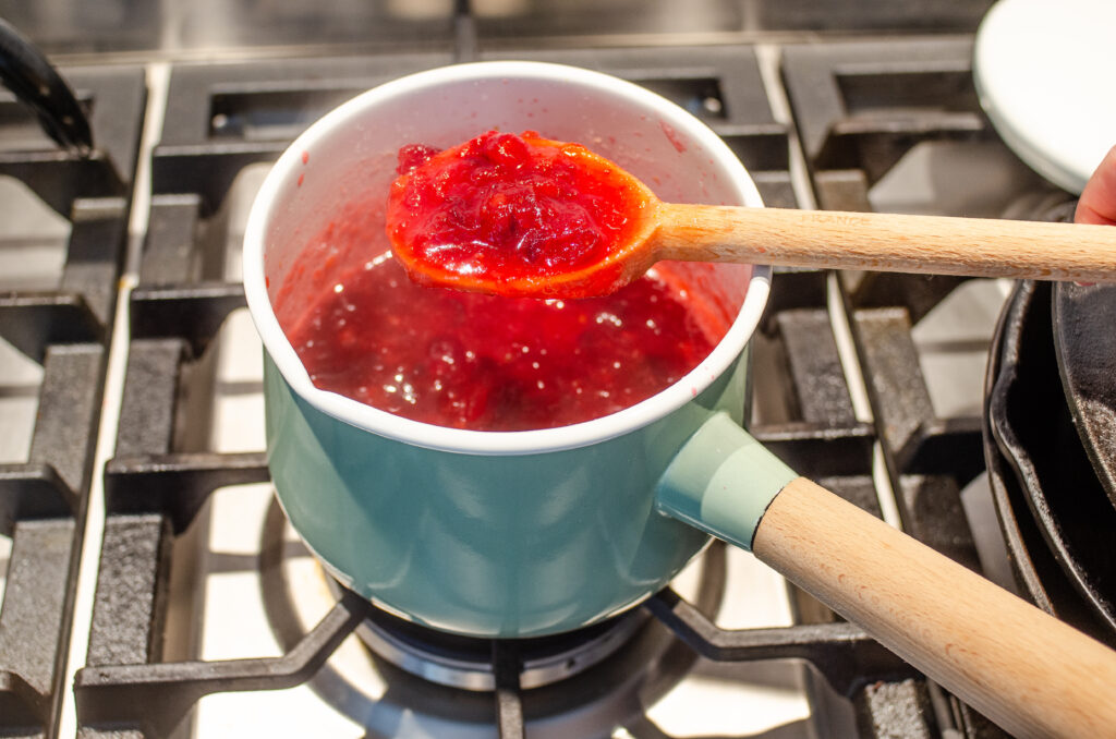Holding a spoonful of the boiled organic cranberry sauce to demonstrate how thick it got after simmering.