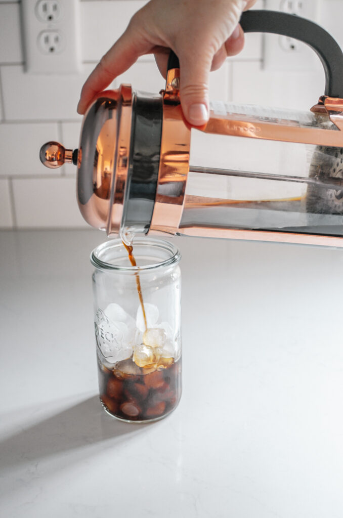 Pouring the French press cold brew over some ice in a cup.