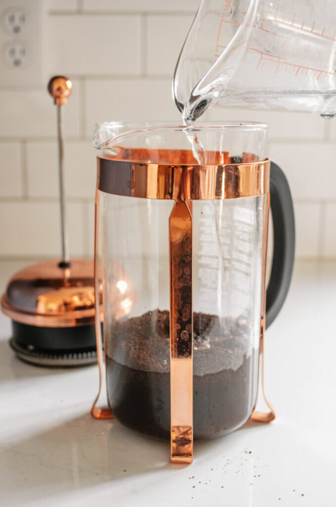 Pouring water over the coffee in the canister of the French press.