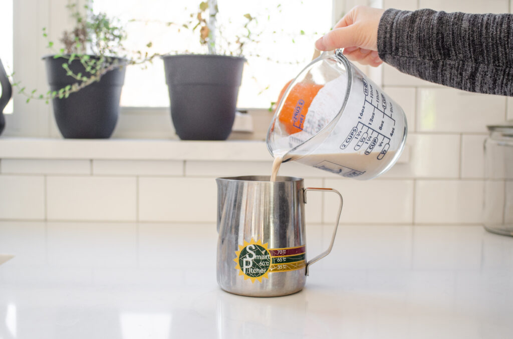 Pouring the chai concentrate and milk into a frothing pitcher.